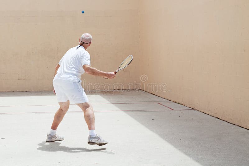 Senior man playing racquetball on an outdoor court. Senior man playing racquetball on an outdoor court.