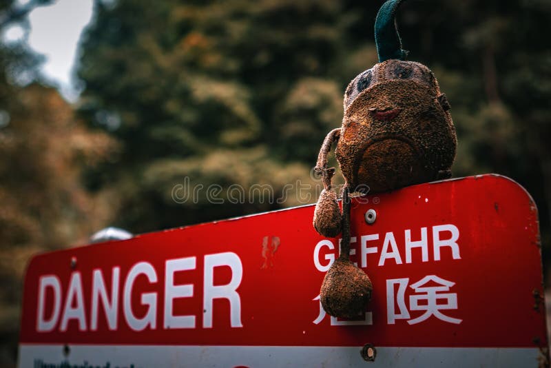 A forlorn stuffed toy rests on a weathered danger sign, an incongruous sight. A forlorn stuffed toy rests on a weathered danger sign, an incongruous sight