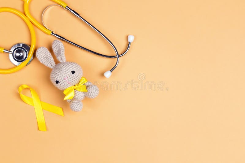 Giocattolo per bambini con consapevolezza del cancro all'infanzia Nastro d'oro e stethoscope su sfondo giallo con spazio fotograf