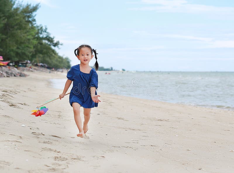 Giocattolo variopinto e funzionamento del mulino a vento della tenuta della neonata sulla spiaggia nella sera fotografie stock libere da diritti Giocattolo variopinto e funzionamento del mulino a vento della tenuta della neonata sulla spiaggia nella sera fotografie stock libere da diritti