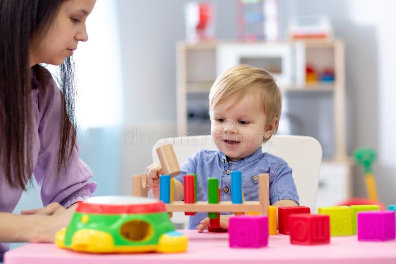 Gioco del bambino e del badante della scuola materna alla tavola nel centro di guardia fotografia stock Gioco del bambino e del badante della scuola materna alla tavola nel centro di guardia fotografia stock