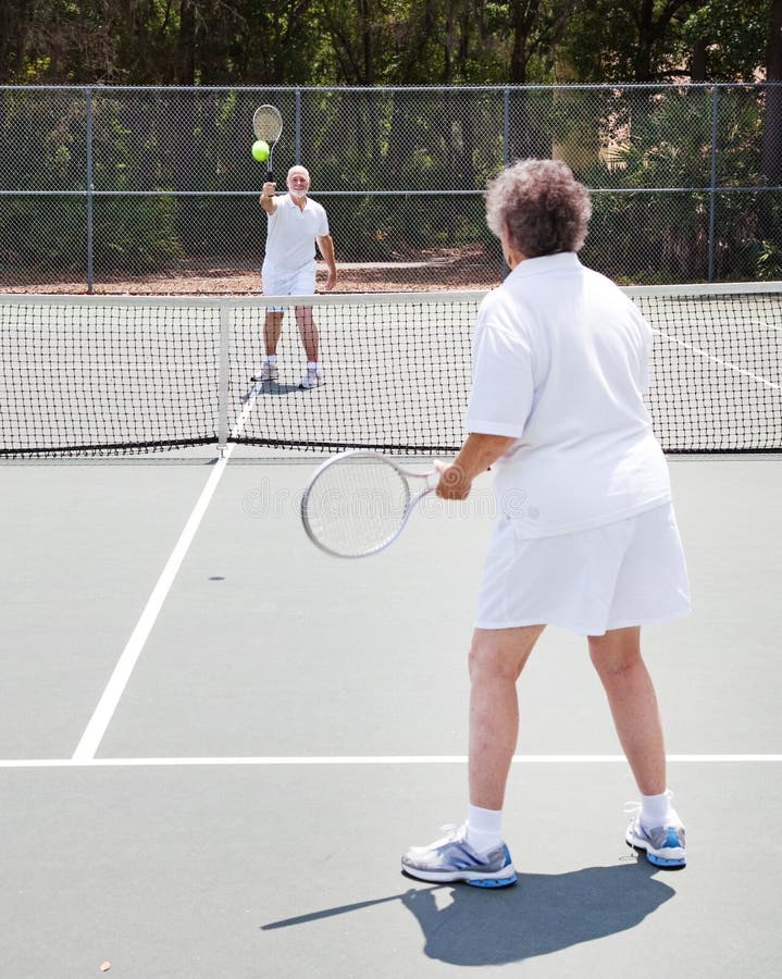 Active senior couple playing tennis together on an outdoor court. Active senior couple playing tennis together on an outdoor court