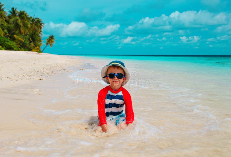 Gioco sveglio del ragazzino con acqua e la sabbia sulla spiaggia fotografia stock libera da diritti Gioco sveglio del ragazzino con acqua e la sabbia sulla spiaggia fotografia stock libera da diritti