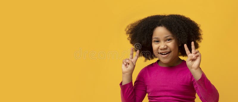 Joyful little afro girl gesturing peace sign and smiling at camera, cheerful child posing over yellow background, panorama with empty space. Joyful little afro girl gesturing peace sign and smiling at camera, cheerful child posing over yellow background, panorama with empty space