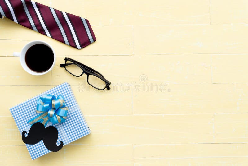 Happy fathers day concept. Red tie, glasses, mustache, gift box and coffee cup on bright yellow pastel wooden table background. Happy fathers day concept. Red tie, glasses, mustache, gift box and coffee cup on bright yellow pastel wooden table background.