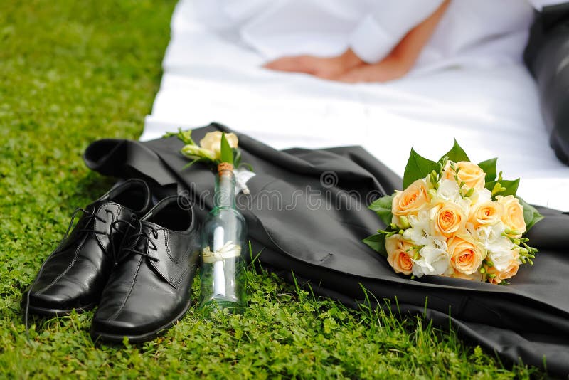 Wedding groom's shoes, jacket, bouquet, a reference in a bottle in the background the bride and groom hands. Wedding groom's shoes, jacket, bouquet, a reference in a bottle in the background the bride and groom hands