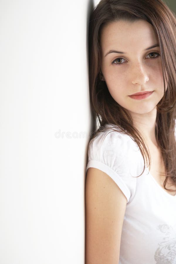 Portrait of a beautiful young adult (teenager) Caucasian woman with light skin and dark brown hair, brown eyes and pink lips, sitting against a wall - copy space. Portrait of a beautiful young adult (teenager) Caucasian woman with light skin and dark brown hair, brown eyes and pink lips, sitting against a wall - copy space