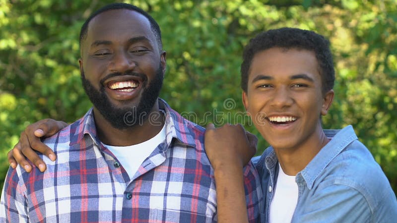 Giovane adolescente afro-americano che abbraccia padre sorridente, ritratto di famiglia felice