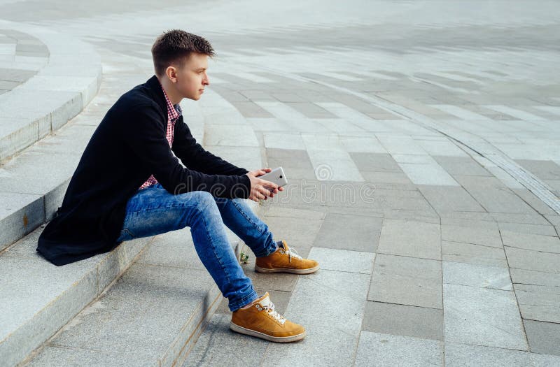 Giovane alla moda in camicia e jeans di plaid che si siedono sulle scale fotografia stock libera da diritti Giovane alla moda in camicia e jeans di plaid che si siedono sulle scale fotografia stock libera da diritti