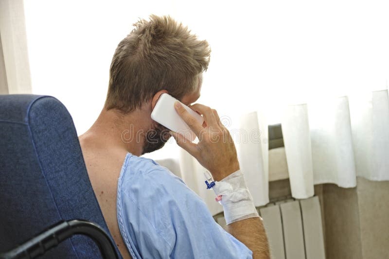Giovane alla stanza di ospedale che porta i pigiami pazienti che si siedono dalla finestra che parla sul telefono cellulare immagini stock Giovane alla stanza di ospedale che porta i pigiami pazienti che si siedono dalla finestra che parla sul telefono cellulare immagini stock