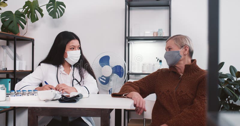 Giovane amichevole e multietnica dottoressa in gabbia di laboratorio, con una paziente anziana che sorride all'ufficio di clinica. fotografia stock
