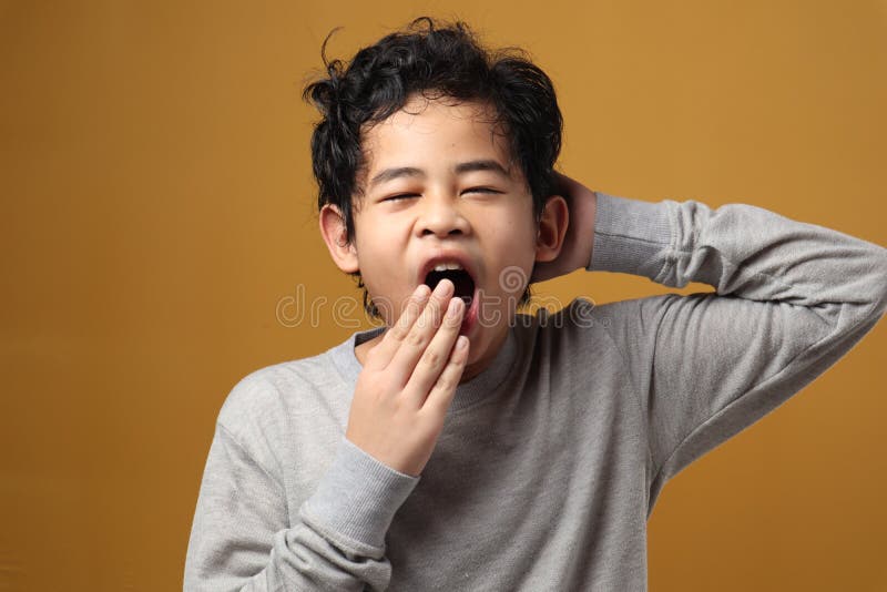 Young Asian boy sleepy and yawning, tired exhausted gesture not enough to rest at night, against yellow background. Young Asian boy sleepy and yawning, tired exhausted gesture not enough to rest at night, against yellow background