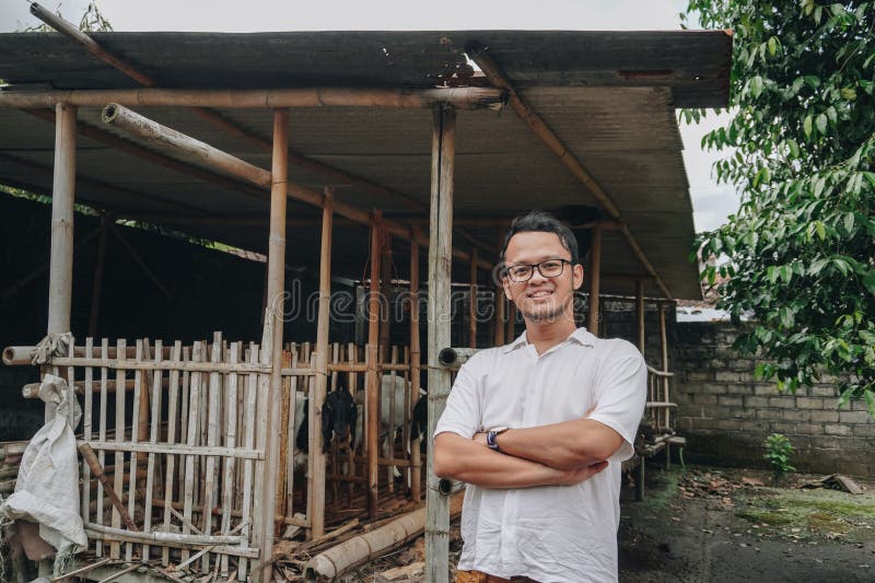 Giovane asiatico eccitato di fronte alla gabbia tradizionale fatta di legno e bambù nella zona rurale indonesiana con capra all'in fotografie stock