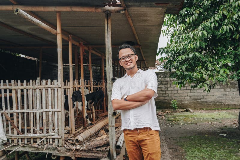 Giovane asiatico eccitato di fronte alla gabbia tradizionale fatta di legno e bambù nella zona rurale indonesiana con capra all'in immagine stock libera da diritti