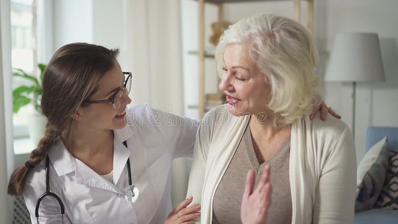 Giovane assistente di medico che visita ed abbracciare donna anziana matura