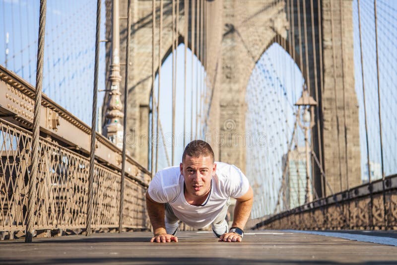 Giovane atleta che fa i piegamenti sulle braccia sul ponte di Brooklyn fotografia stock libera da diritti Giovane atleta che fa i piegamenti sulle braccia sul ponte di Brooklyn fotografia stock libera da diritti