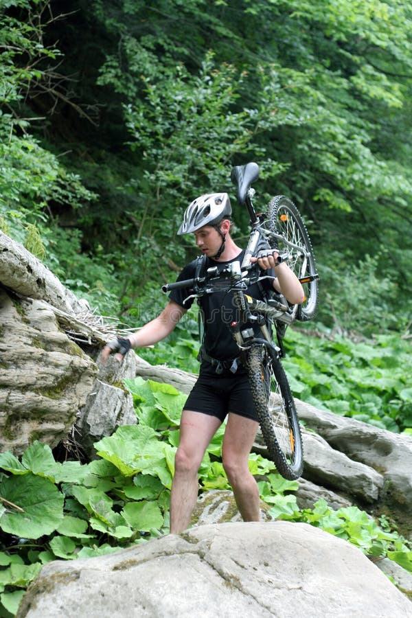 Giovane atleta che sta su una roccia con la bicicletta fotografia stock Giovane atleta che sta su una roccia con la bicicletta fotografia stock