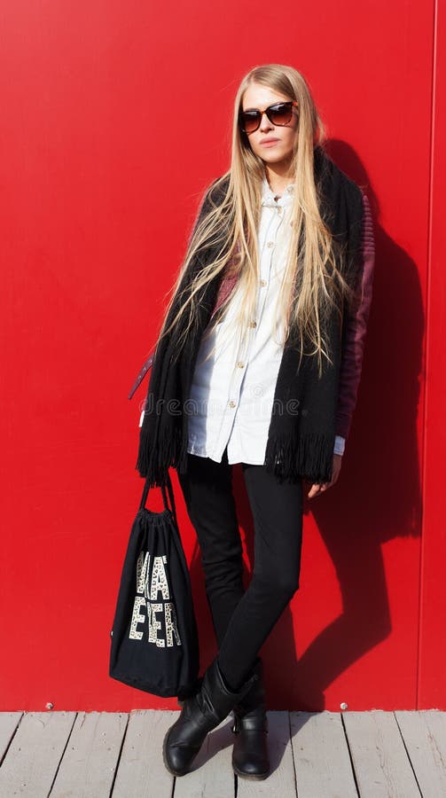 Giovane attrezzatura d'avanguardia bionda stupefacente di usura di donna, vetri alla moda Su fondo rosso, all'aperto Streetstyle immagine stock Giovane attrezzatura d'avanguardia bionda stupefacente di usura di donna, vetri alla moda Su fondo rosso, all'aperto Streetstyle immagine stock