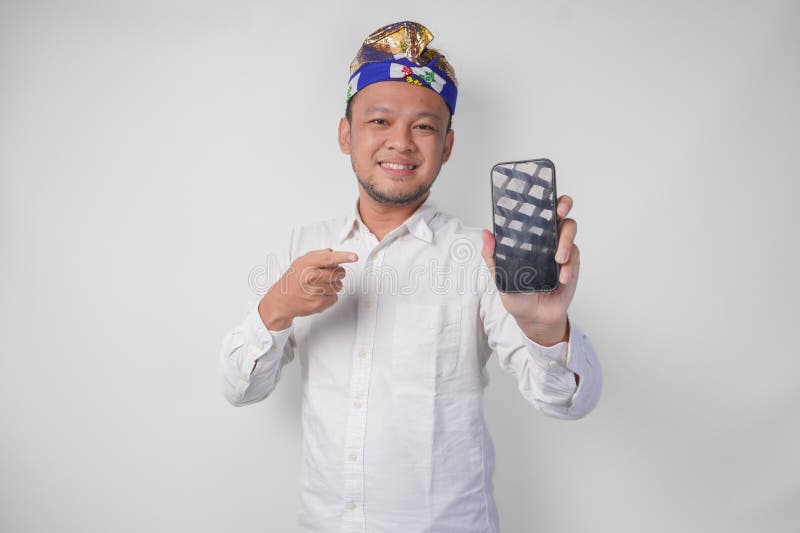 Giovane balinese sorridente con camicia bianca e taccuino tradizionale puntando sul suo smartphone presentandone una in bianco fotografia stock libera da diritti