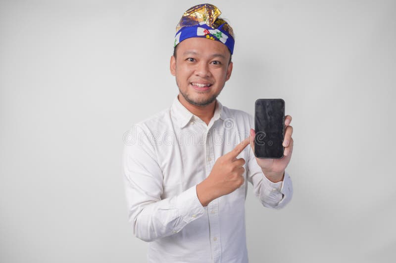 Giovane balinese sorridente con camicia bianca e taccuino tradizionale puntando sul suo smartphone presentandone una in bianco immagini stock