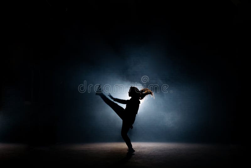 Giovane ballerino con alto da fare rizzare i capelli lungo la sua gamba sulla fase scura fotografia stock libera da diritti Giovane ballerino con alto da fare rizzare i capelli lungo la sua gamba sulla fase scura fotografia stock libera da diritti