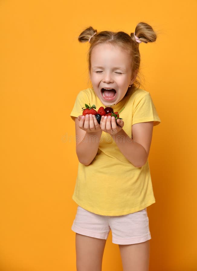 Giovane bambino della neonata con una manciata di frutti di bacche in sue mani delle palme che grida con la felicità o nello spav fotografie stock Giovane bambino della neonata con una manciata di frutti di bacche in sue mani delle palme che grida con la felicità o nello spav fotografie stock