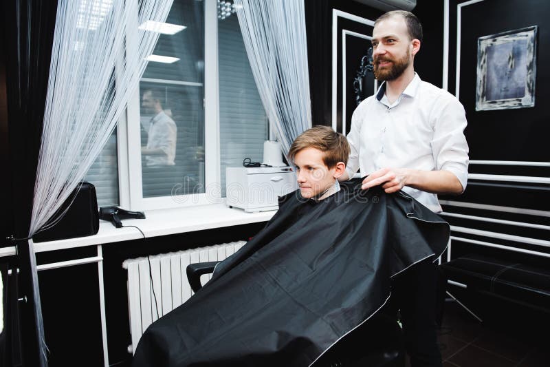 Giovane barbiere bello che fa taglio di capelli del ragazzo sveglio in parrucchiere fotografie stock Giovane barbiere bello che fa taglio di capelli del ragazzo sveglio in parrucchiere fotografie stock