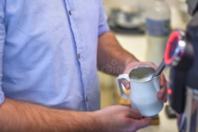 Giovane barista che cuoce a vapore latte in lanciatore bianco sulla macchina di caffè espresso fotografia stock libera da diritti Giovane barista che cuoce a vapore latte in lanciatore bianco sulla macchina di caffè espresso fotografia stock libera da diritti