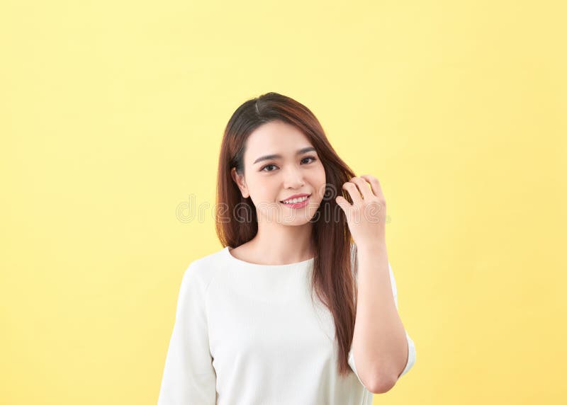 Giovane bella donna asiatica che sorride e che tocca per lisciare i suoi capelli su fondo giallo fotografie stock libere da diritti