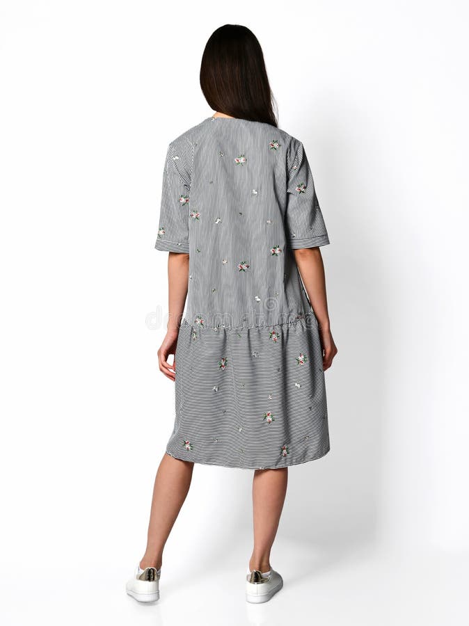 Giovane bella donna che posa nella vista posteriore del nuovo di progettazione delle bande vestito casuale dalla molla su grigio immagine stock Giovane bella donna che posa nella vista posteriore del nuovo di progettazione delle bande vestito casuale dalla molla su grigio immagine stock