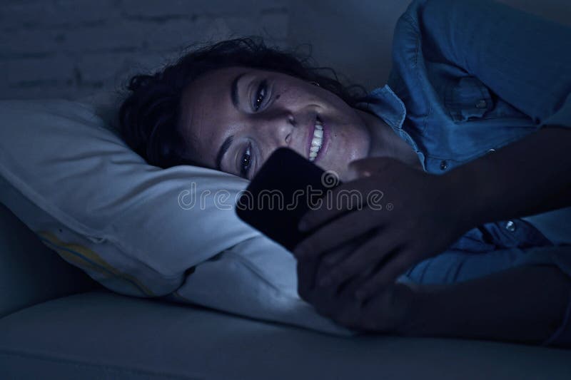 Giovane bella donna che si trova sullo strato domestico facendo uso del tex del telefono cellulare immagini stock Giovane bella donna che si trova sullo strato domestico facendo uso del tex del telefono cellulare immagini stock