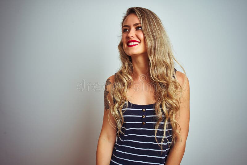 Giovane bella donna con una camicia in piedi su uno sfondo bianco isolato e guardata a lato col sorriso sul viso fotografia stock libera da diritti