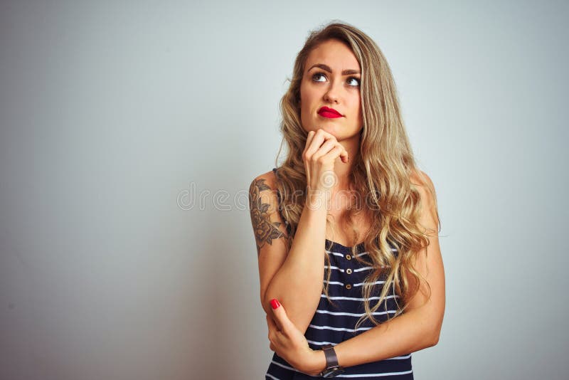 Giovane bella donna con una camicia a strisce, in piedi su fondo bianco isolato e preoccupata per una domanda che si preoccupa immagine stock libera da diritti