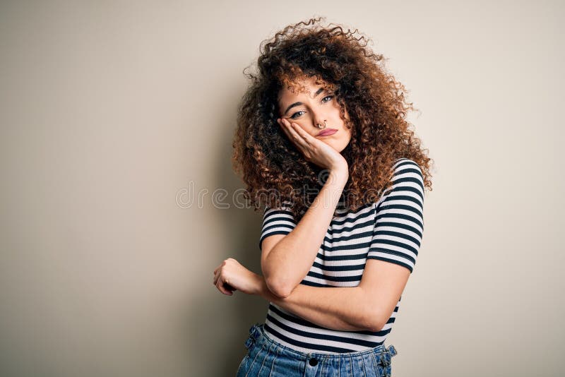Giovane bella donna dai capelli ricci e piercing con camicia a strisce casual pensata stanca e annoiata dalla depressione fotografia stock