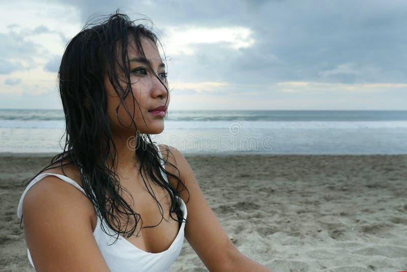 Giovane bella ragazza asiatica con capelli bagnati alla spiaggia di tramonto che guarda nella distanza premurosa e pensierosa fotografia stock libera da diritti Giovane bella ragazza asiatica con capelli bagnati alla spiaggia di tramonto che guarda nella distanza premurosa e pensierosa fotografia stock libera da diritti