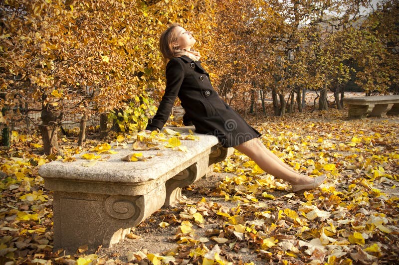 A young beautiful girl enjoying warm autumn sun on a stone bench. A young beautiful girl enjoying warm autumn sun on a stone bench