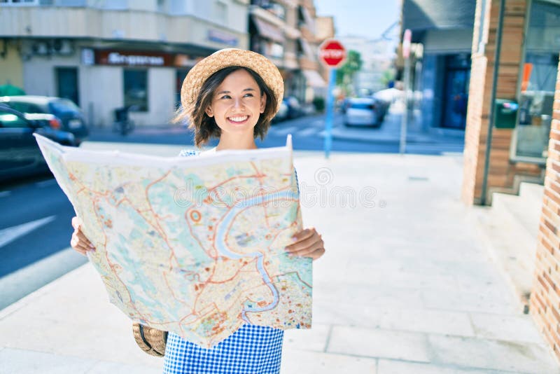 Giovane bella ragazza che sorride felice tenendo una mappa della città in strada immagine stock