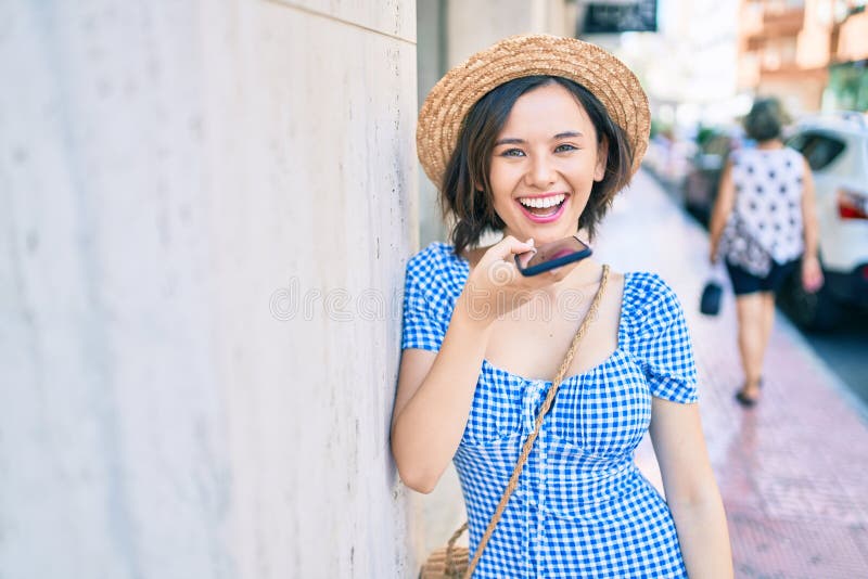 Giovane bella ragazza che sorride felice usando lo smartphone appoggiato al muro per strada immagini stock libere da diritti