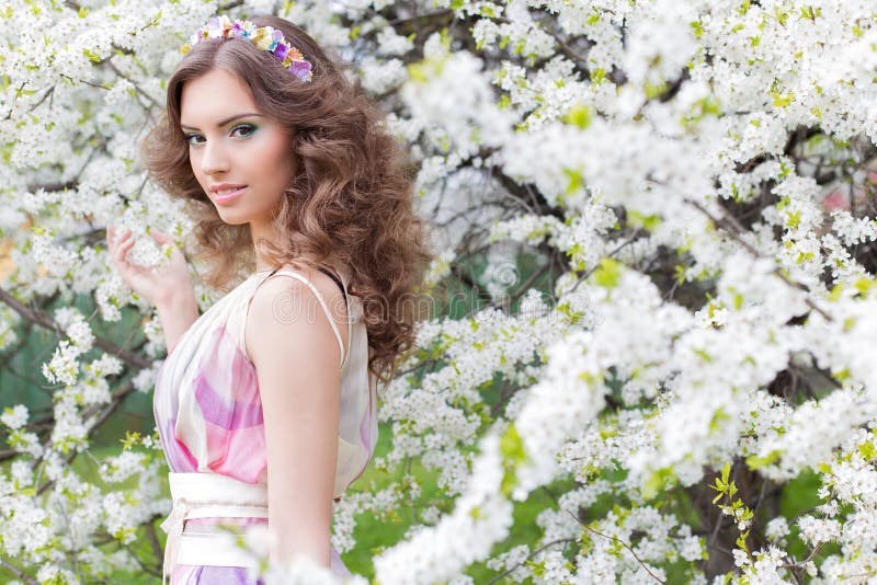 Giovane bella ragazza elegante abbastanza delicata con capelli fertili con un orlo dei fiori brillantemente colorati in un giardi immagine stock