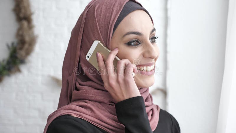 Giovane bella ragazza indiana nel hijab che distoglie lo sguardo, esaminando macchina fotografica, sorridendo, parlante sullo sma