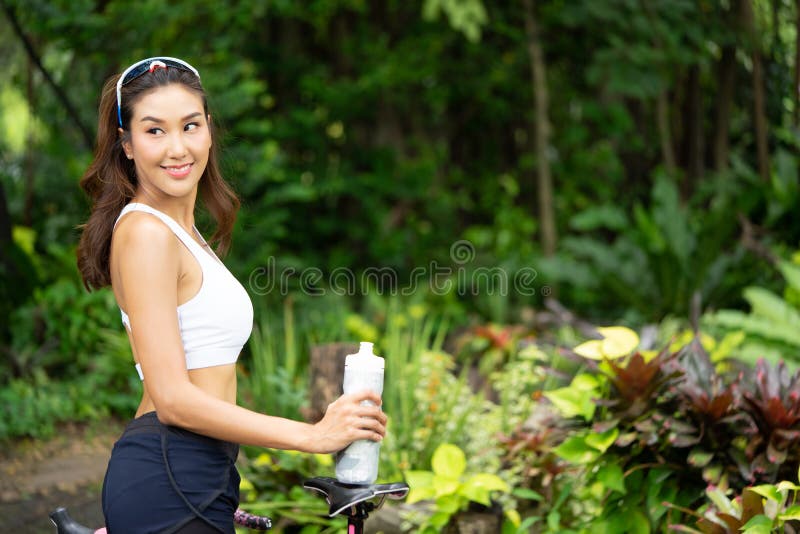 Giovane bottiglia sorridente della tenuta della donna di sport di acqua nel parco immagine stock Giovane bottiglia sorridente della tenuta della donna di sport di acqua nel parco immagine stock