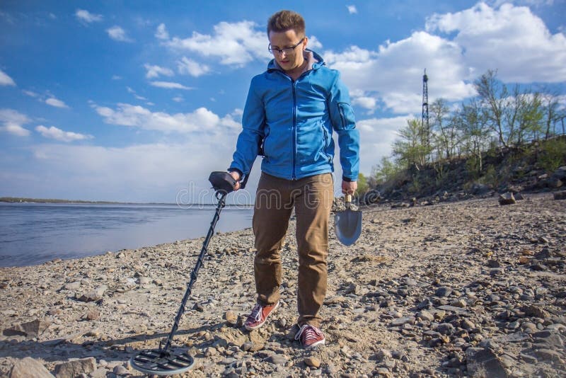 A young treasure hunter is looking for treasures on the riverbank with a metal detector. A young treasure hunter is looking for treasures on the riverbank with a metal detector