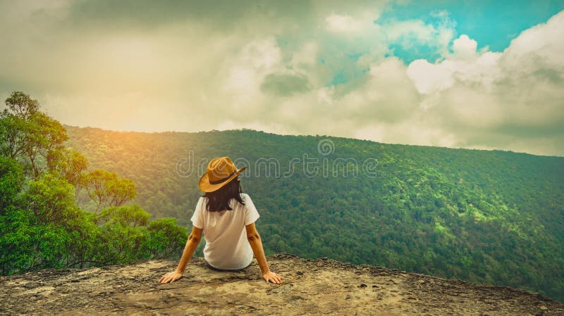 Giovane cappello d'uso di viaggio della donna e sedersi sulla cima della scogliera della montagna con l'umore di rilassamento Via