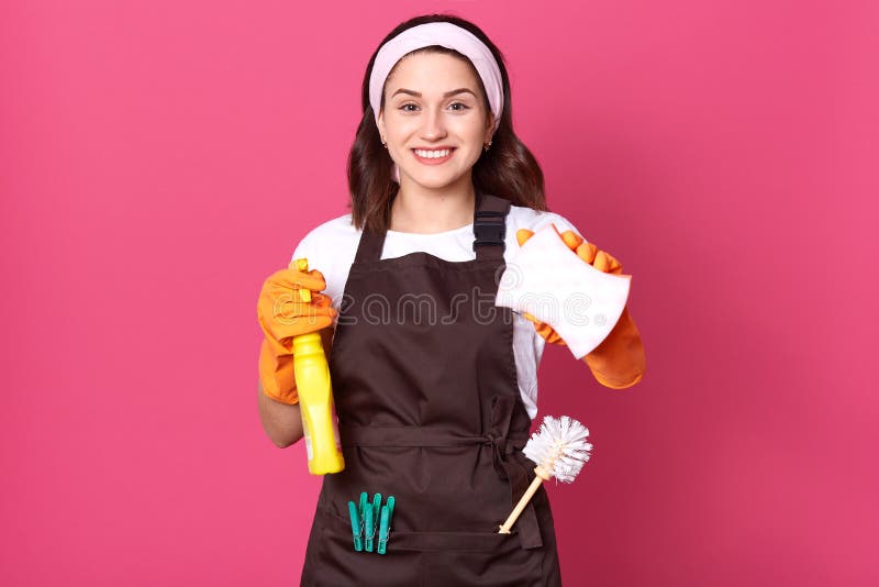 Giovane casalinga sorridente che indossa una fascia per capelli, grembiule marroni e casual bianco a shiert, posta isolata sullo immagini stock libere da diritti Giovane casalinga sorridente che indossa una fascia per capelli, grembiule marroni e casual bianco a shiert, posta isolata sullo immagini stock libere da diritti