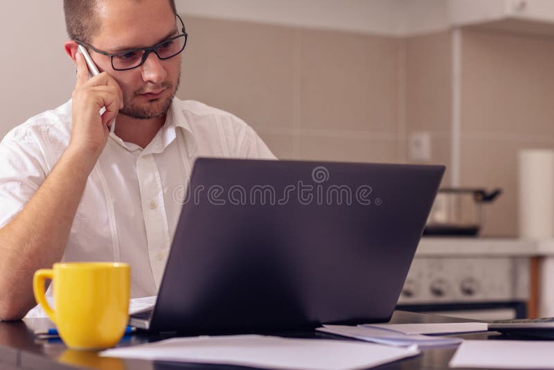 Giovane che lavora con il computer mentre parlando sul telefono a casa fotografia stock Giovane che lavora con il computer mentre parlando sul telefono a casa fotografia stock