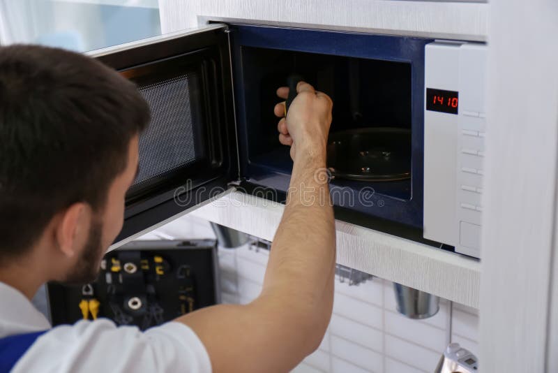 Giovane che ripara forno a microonde, fotografia stock Giovane che ripara forno a microonde, fotografia stock