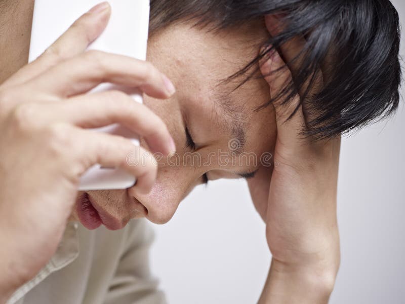 Close-up of an asian young man looking sad and depressed while talking on cellphone. Close-up of an asian young man looking sad and depressed while talking on cellphone.