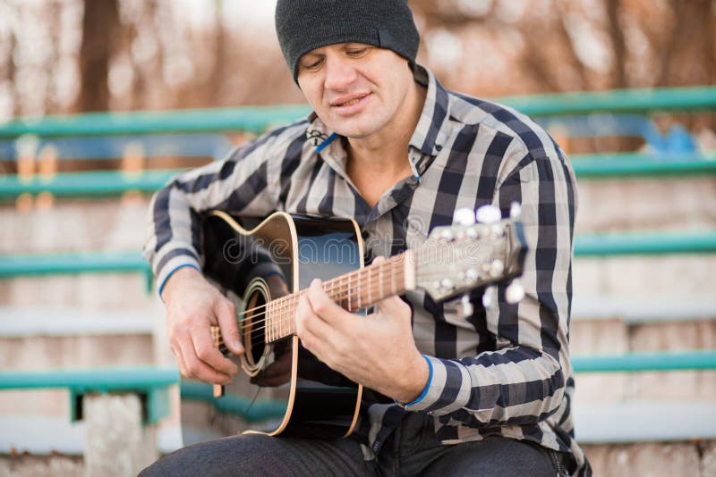 Giovane che si siede sui punti che giocano chitarra e che cantano fotografia stock libera da diritti Giovane che si siede sui punti che giocano chitarra e che cantano fotografia stock libera da diritti