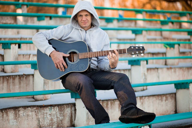 Giovane che si siede sui punti che giocano chitarra e che cantano immagine stock Giovane che si siede sui punti che giocano chitarra e che cantano immagine stock