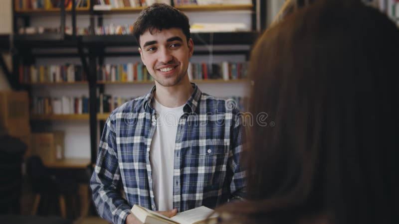 Giovane che sorride mentre parla in una accogliente biblioteca con scaffali pieni di libri stock footage
